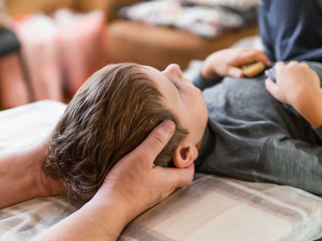 A chiropractor gently examining a young child's back in a bright, family-friendly clinic room.